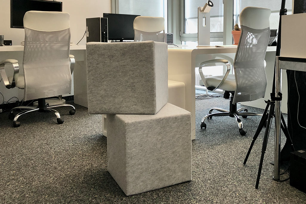 Two light gray acoustic cubes stacked on top of each other in a modern office.