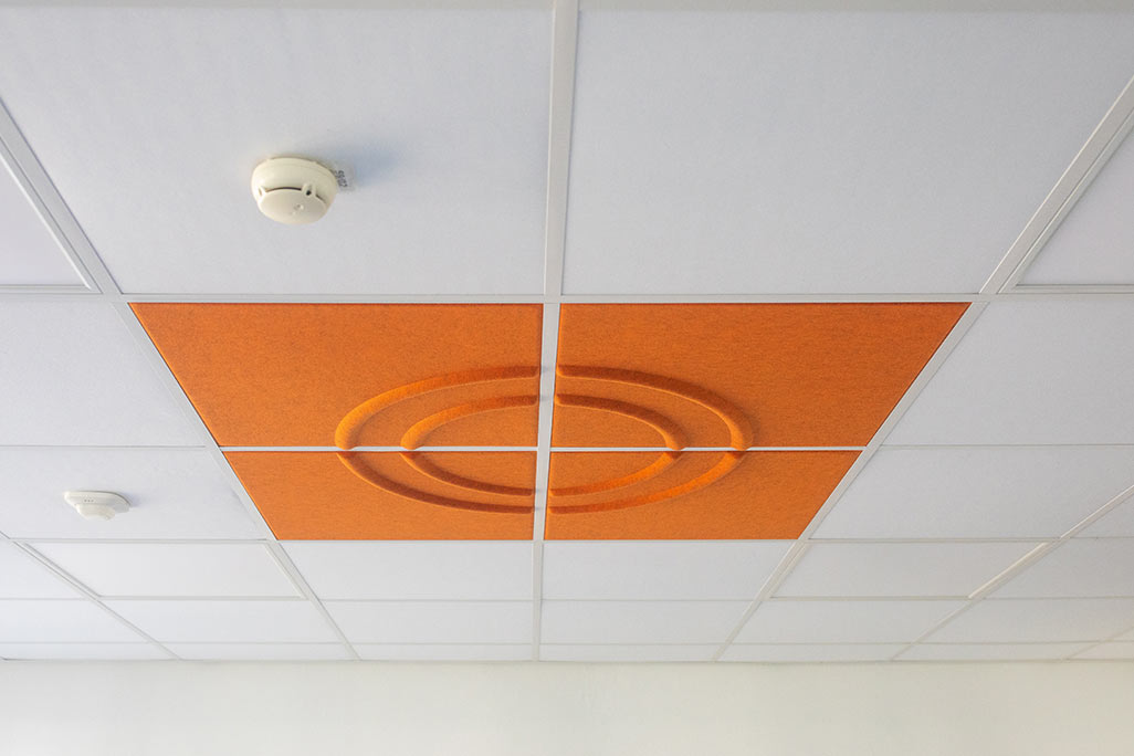 Section of a standard grid ceiling with inlaid soni COMFORT SD acoustic absorbers in white and soni COLOR Design in orange.