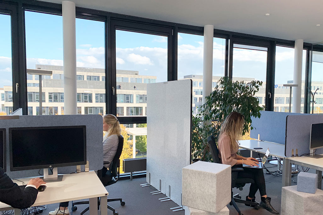 Modern office with large windows, desk, acoustic absorbers on the wall and partitions on the desks