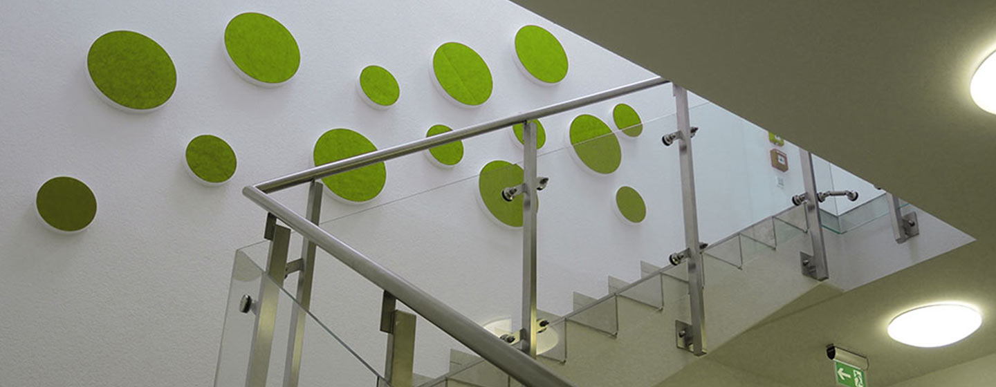 14 sound absorbers in the shape of a circle (soni ELEMENT CIRCLE) in the color green mounted on a white wall in a modern stairwell.